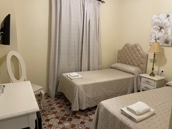 A bedroom with two beds, a desk, a chair, a lamp, and a painting on the wall. - Hostal Flor de Lis - Lojo (Conil de la Frontera)