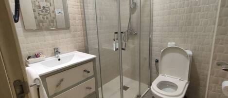 Un baño con cabina de ducha de vidrio, inodoro blanco y lavabo con espejo superior.