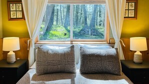 A bedroom with a large window, two bedside lamps, and a bed with two pillows. - Pinecrest Family Summer Retreat Kid Playroom and Game Room (Island Park)