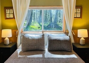 Een slaapkamer met een groot raam, twee bedlampen en een bed met twee kussens.