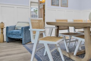 Ein Essbereich mit weißen Stühlen und einem runden Tisch, einem blauen Sofa und einem gemusterten Teppich.