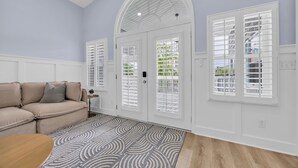 Ein Zimmer mit einem beigefarbenen Sofa, einem gemusterten Teppich und einer weißen Tür mit Fensterläden.