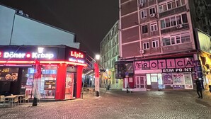Una calle iluminada de noche con un edificio que muestra un letrero 'Diner' y un letrero 'Tropica'.
