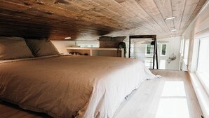 A spacious bedroom with a large bed, wooden ceiling, and a view of the outdoors. - Shadow’s Hideaway - Tiny Home w/ Fire Pit + Views (Cleveland)