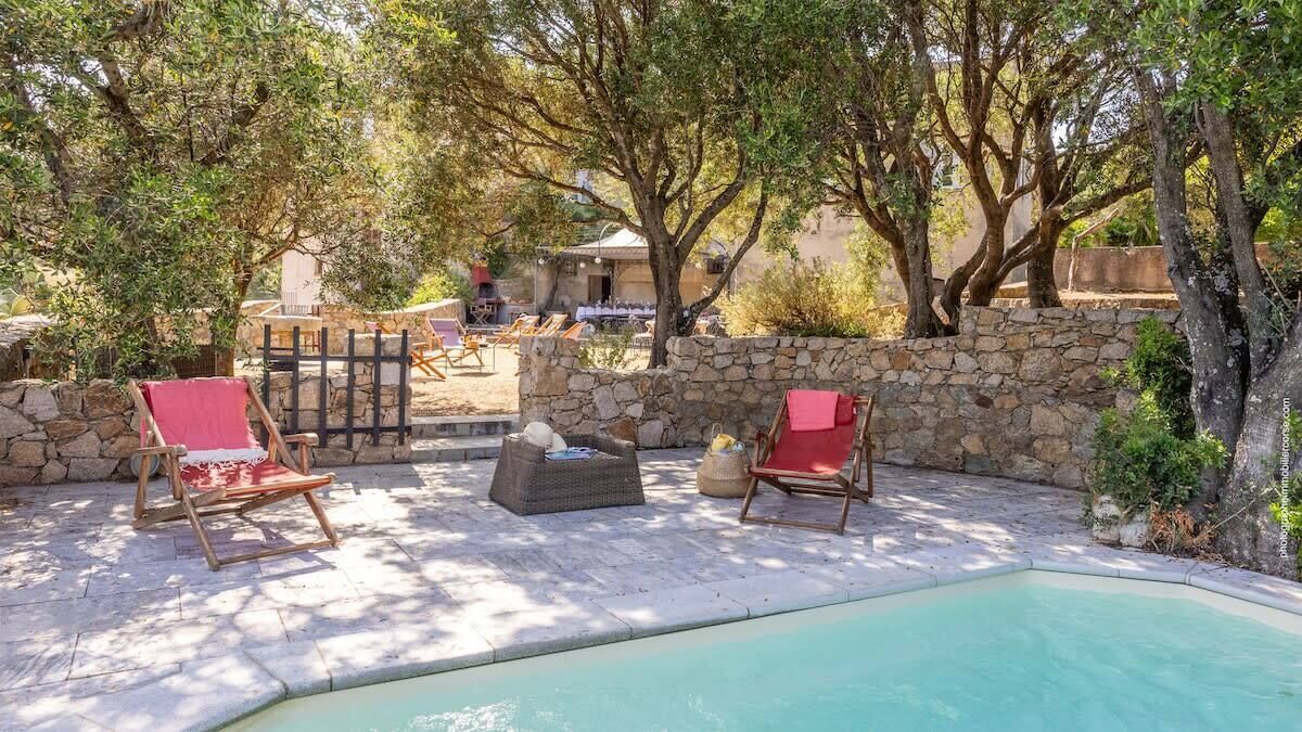 A poolside area with stone walls and wooden lounge chairs.