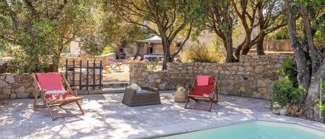 A poolside area with stone walls and wooden lounge chairs.