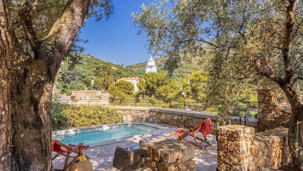 Zona de piscina con asientos de piedra y vistas a un edificio blanco en una colina.