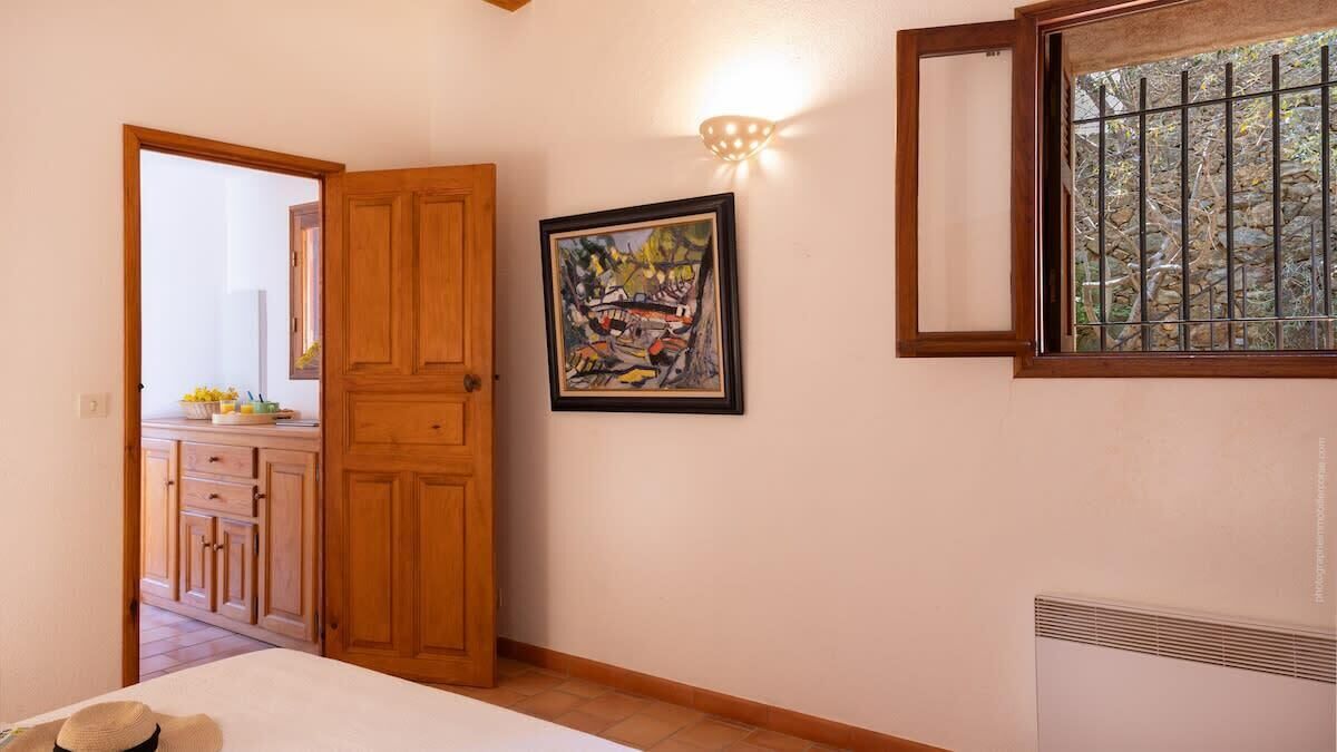 A bedroom with a wooden door, a framed painting, a window with bars, and a radiator.