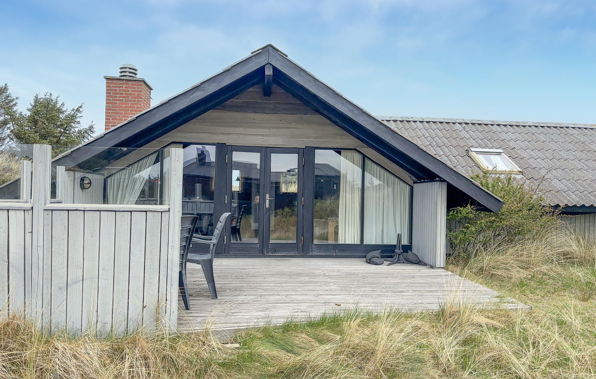 Et moderne hus med stor glasdør, træterrasse og murstens skorsten.