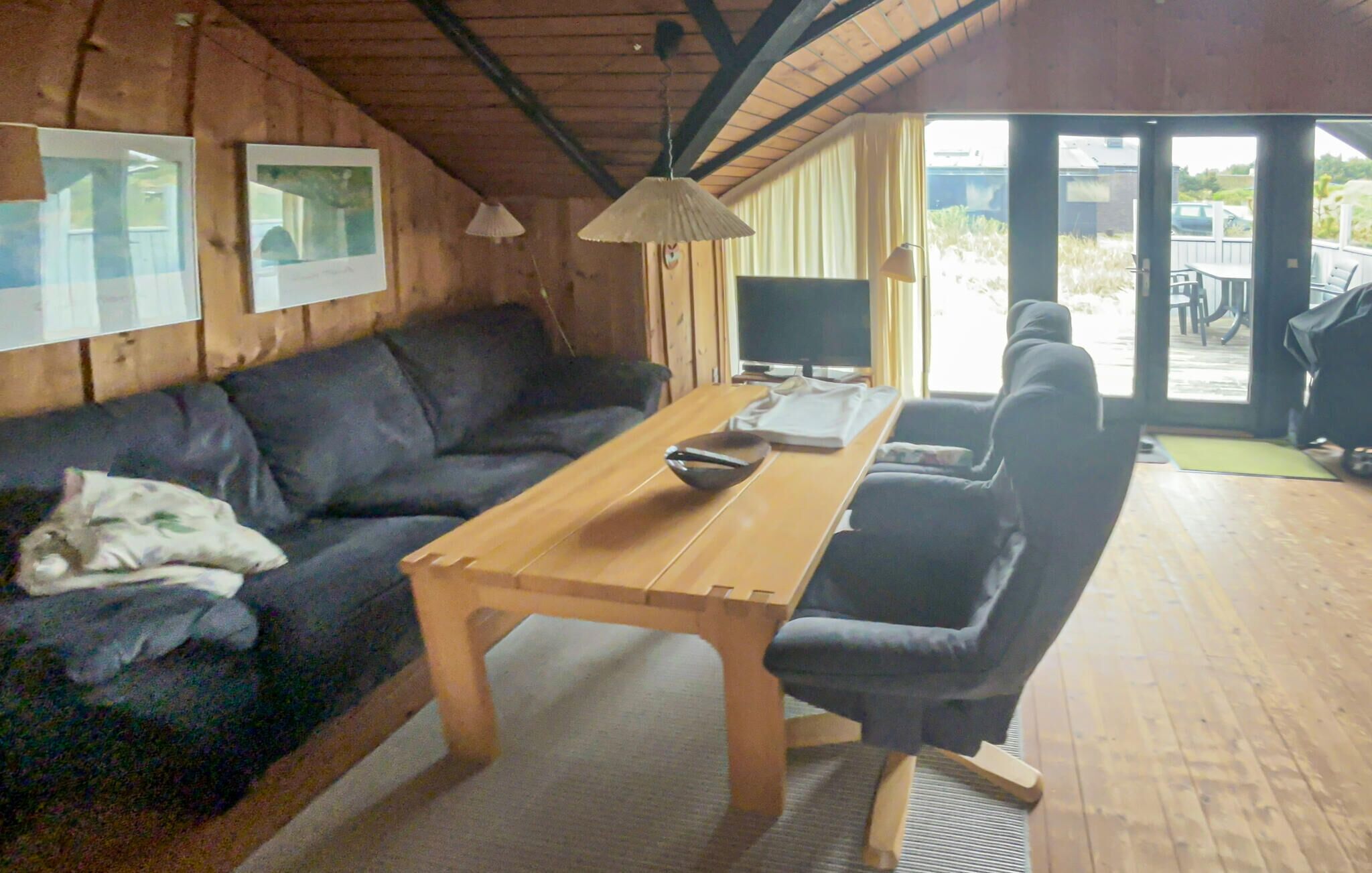 A cozy room with a wooden table, a black sofa, and a TV.