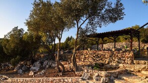 A stone structure with a wooden pergola, surrounded by trees and rocky terrain. - Luxurious home in Sali with WiFi (Sali)