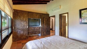 A bedroom with a large bed, wooden paneling, a flat-screen TV, and a window with bars. - TOPOWA CLUB HOUSE RESORT (Giron)