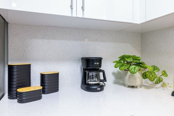 Una cocina con cafetera, platos apilados y una planta en maceta.