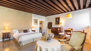 Una habitación de hotel con una cama, una mesa redonda con un florero, una silla, un escritorio y una lámpara.