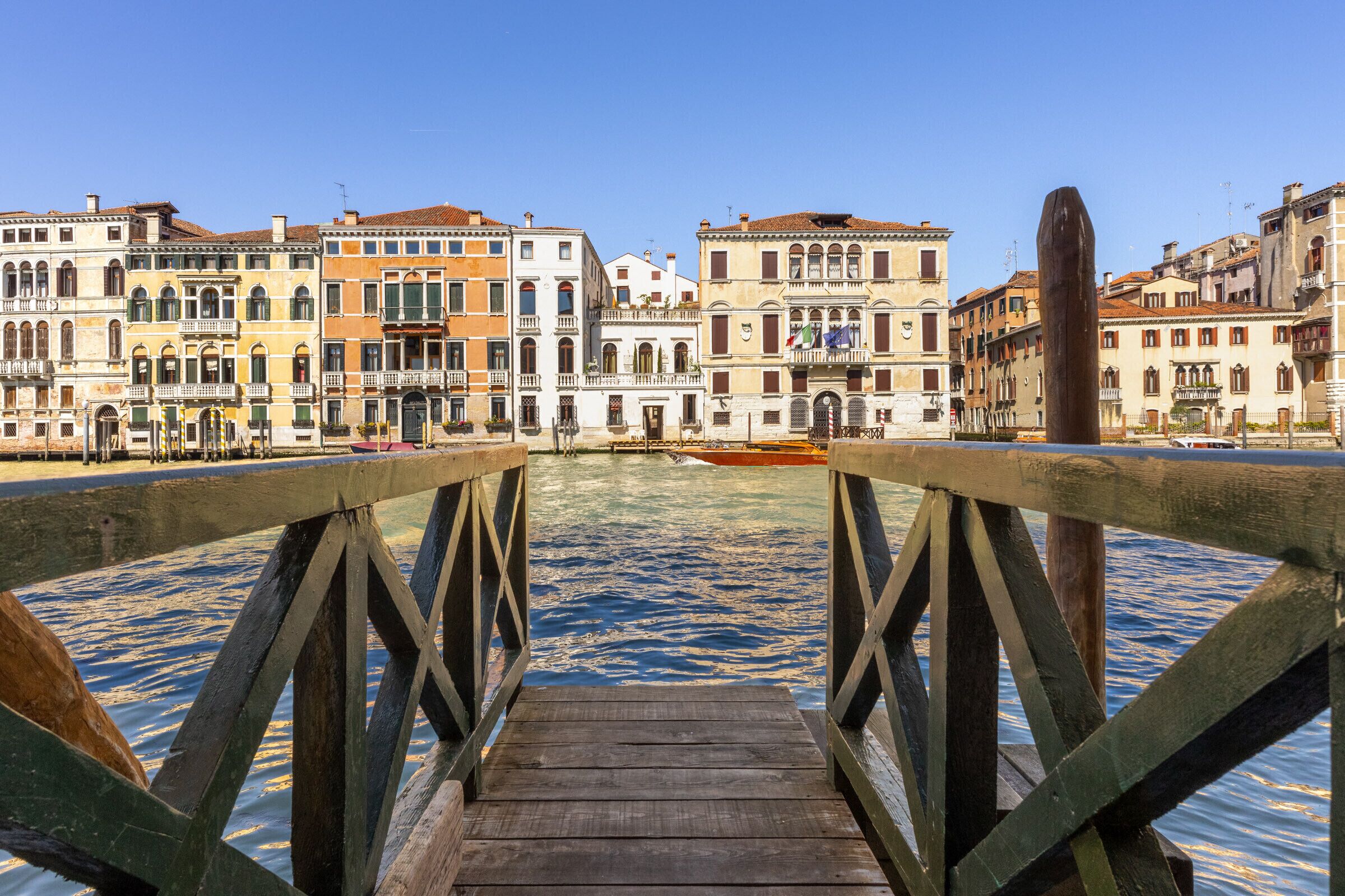 A wooden pier leading to a canal with historic buildings in the background.