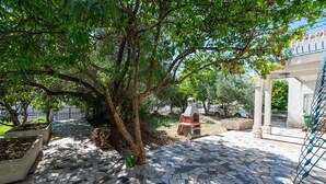 A stone-paved courtyard with a large tree, a barbecue grill, and a metal bench. - Cozy apartment in Trogir with WiFi (Trogir)