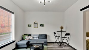 A modern living room with a grey sofa, a black coffee table, and a small dining area with two chairs and a table. - Joe's Place in Historic Wallace, Idaho (Wallace)