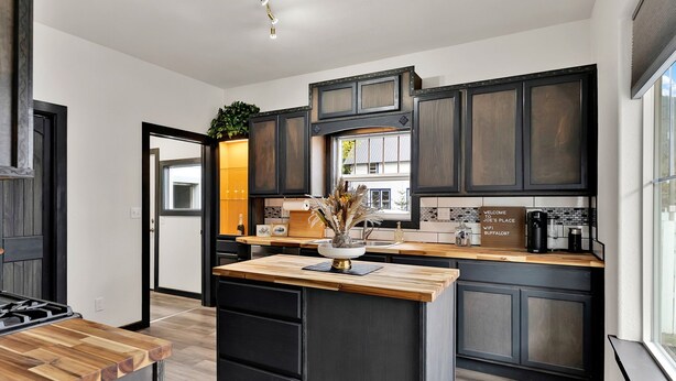 A modern kitchen with dark cabinetry, a wooden island, and a view of the outside. - Joe's Place in Historic Wallace, Idaho (Wallace)