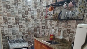 A compact kitchen with a gas stove, oven, wooden cabinets, a granite countertop, and a refrigerator. - Suíte Familiar em Paraty  (Paraty)
