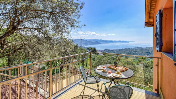Un balcón con una mesa para dos, con vistas a un paisaje pintoresco que incluye montañas y un cuerpo de agua.
