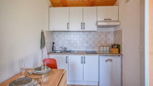 Cocina compacta con armarios blancos, un lavamanos, un refrigerador pequeño y una zona de comedor con una mesa para dos.