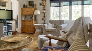 A cozy living room with a television, wicker furniture, a striped armchair, and a large window with a view of trees. - 3 bedroom cozy home in Tingstäde (Tingstäde)