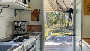 A kitchen with a stove, coffee maker, and a view of a wooden deck and trees. - 3 bedroom cozy home in Tingstäde (Tingstäde)