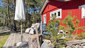 A red cabin with a wooden deck, surrounded by pine trees and a white umbrella. - 3 bedroom cozy home in Tingstäde (Tingstäde)