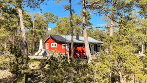 A red cabin with a black roof surrounded by trees. - 3 bedroom cozy home in Tingstäde (Tingstäde)