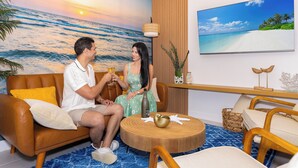 A living room with a sunset mural, a flat-screen TV, and a round wooden coffee table.