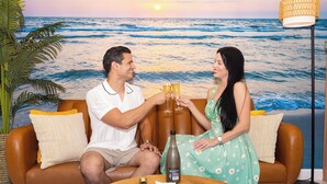 A couple seated on a brown leather sofa with a backdrop of a beach scene.