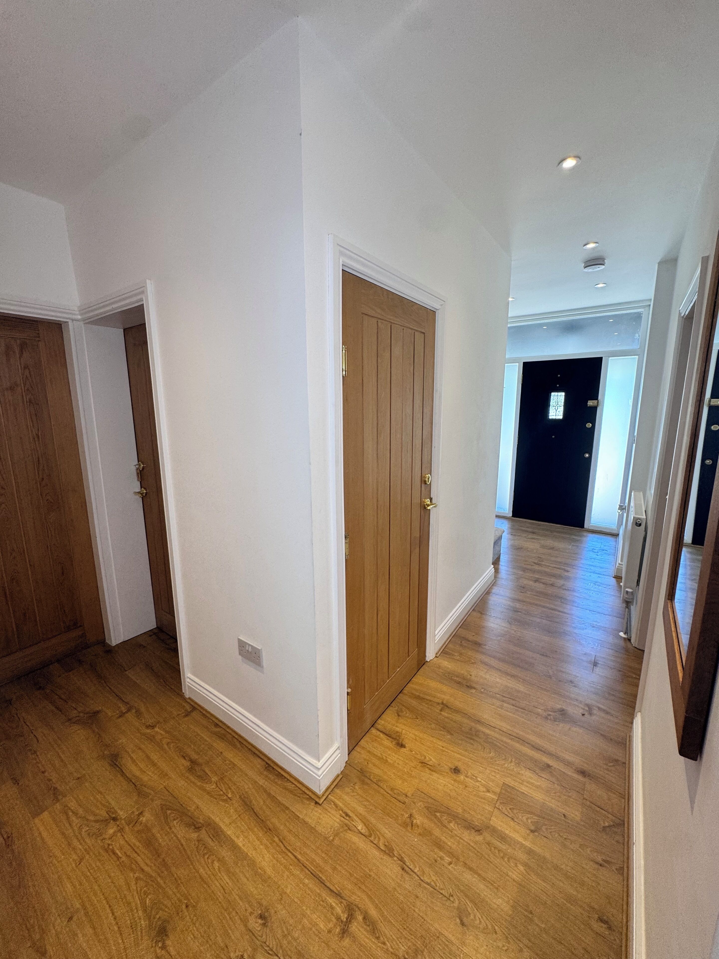 A hallway with wooden flooring, white walls, and a wooden door.