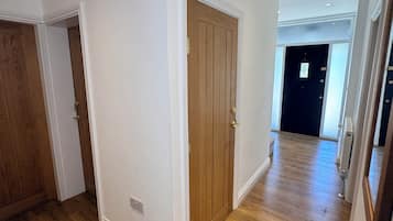 A hallway with wooden flooring, white walls, and a wooden door.