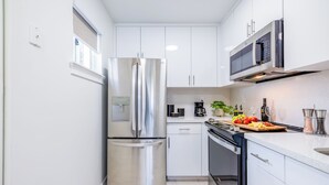Eine moderne Küche mit Edelstahlgeräten, weißen Schränken und einer Arbeitsplatte mit Früchten und einer Kaffeemaschine.