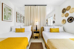 Hotellihuone, jossa on kaksi sänkyä, yöpöytä, lamppu ja koristeellinen seinätaideteos.