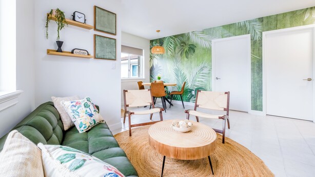 Ein modernes Wohnzimmer mit einem grünen Sofa, einem runden Holztisch und einem Essbereich mit Stühlen und einem Tisch.