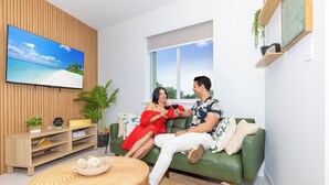 Ein modernes Wohnzimmer mit einem grünen Sofa, einem Holztisch und einem Flachbildfernseher, der eine Strandansicht zeigt.
