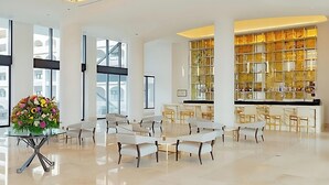 Um hall amplo com uma mesa de vidro, cadeiras brancas e um arranjo floral grande.
