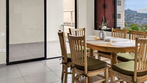 A dining area with a round wooden table, six wooden chairs with green cushions, and a vase with flowers.