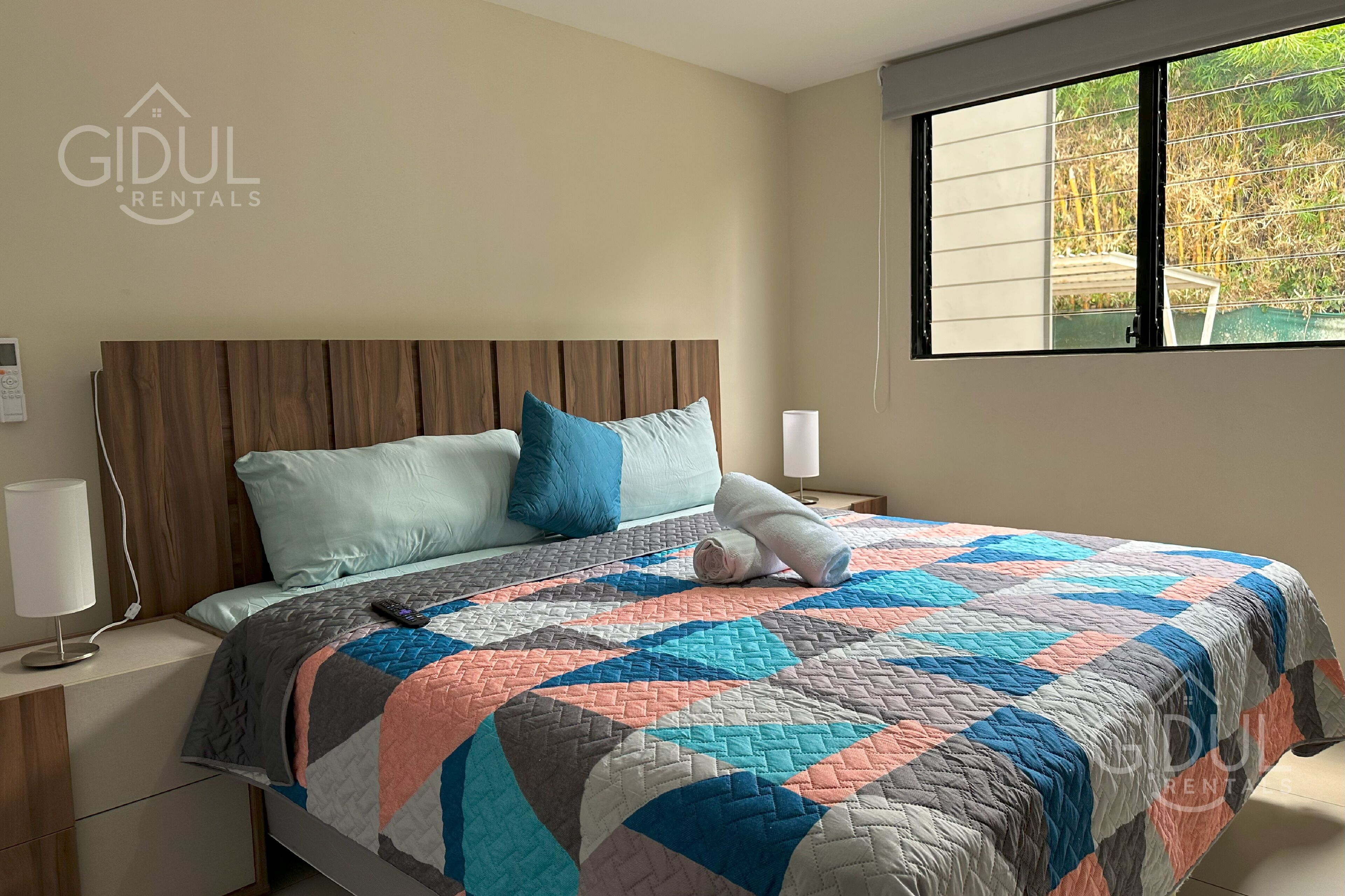 Un dormitorio con cabecera de madera, colcha acolchada y ventana con vistas a bambú.