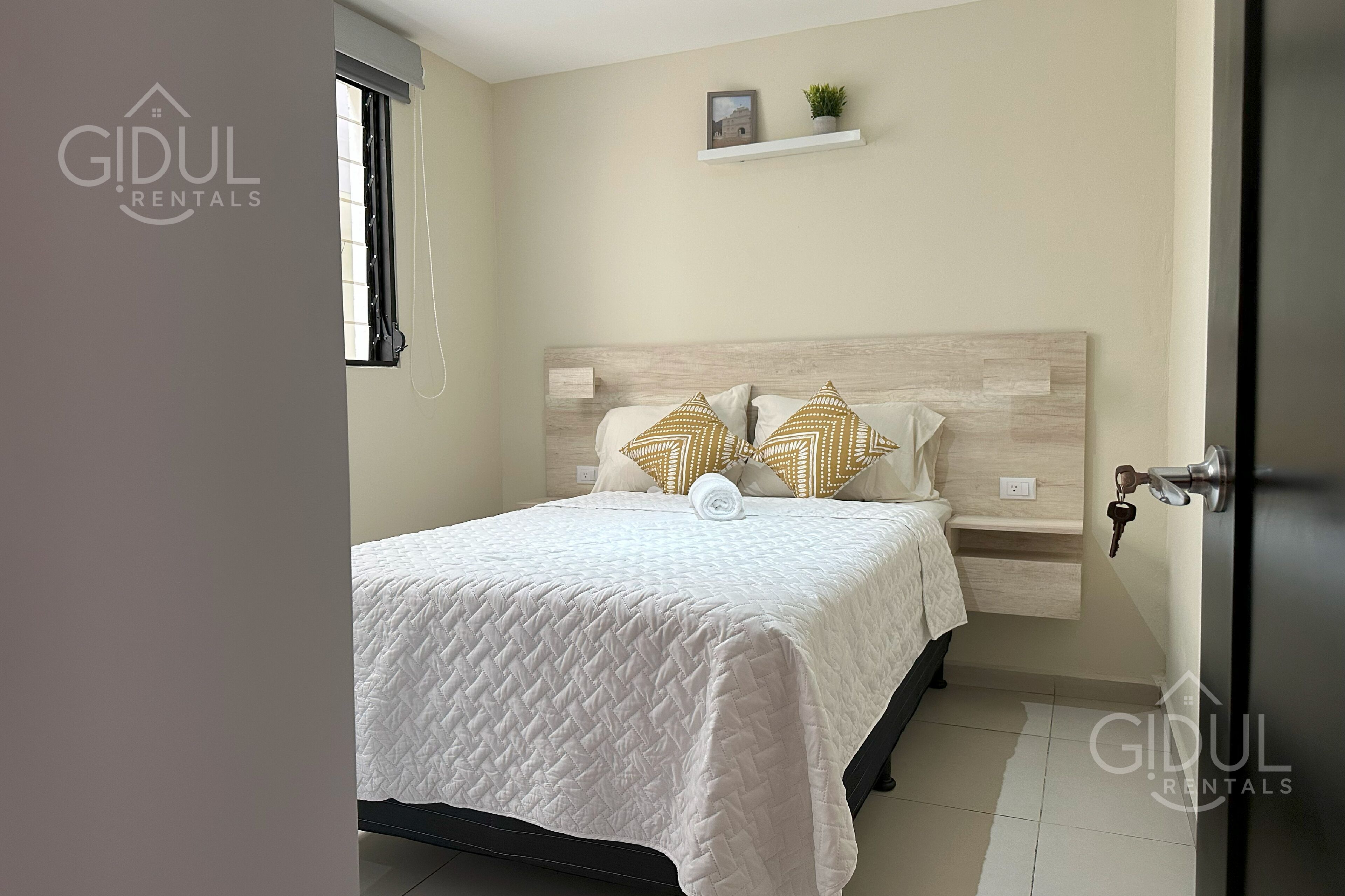 Un dormitorio con cama, cabecera, estante con una planta y una puerta con llave.