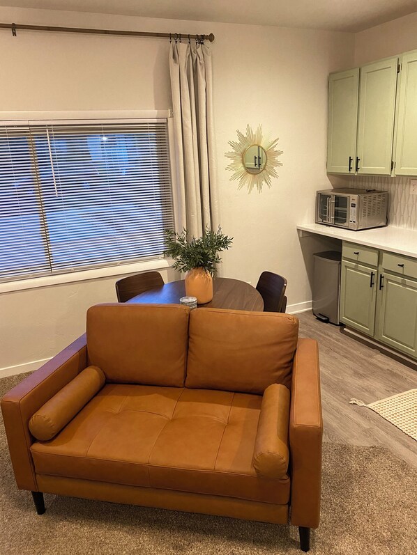 A living room with a brown sofa, a dining table with chairs, a potted plant, and a kitchen area with cabinets and a microwave. - Cozy studio in Washington with WiFi, AC, close to restaurants & shopping. (Washington)
