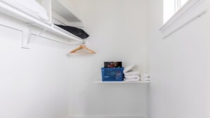 Un placard blanc avec des étagères, une tringle à vêtements et un panier bleu.