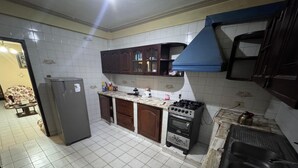 Eine Küche mit weißen Fliesen, Holzschränken, einem Gasherd und einem Kühlschrank.