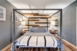Camera da letto con letto a baldacchino, poggiatesta in legno intarsiato e copripiumino grigio con motivo geometrico bianco e nero.