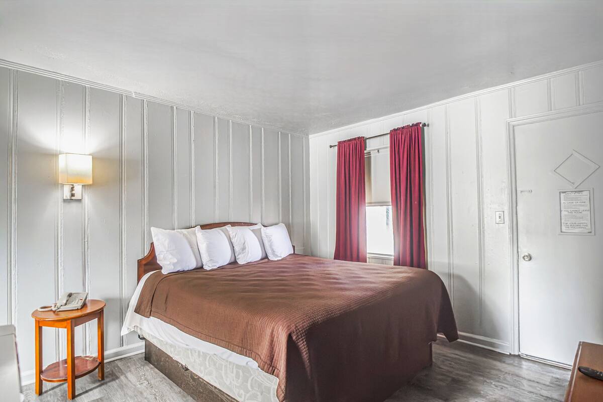 A bedroom with a large bed, a bedside table with a lamp, and a door with a notice.