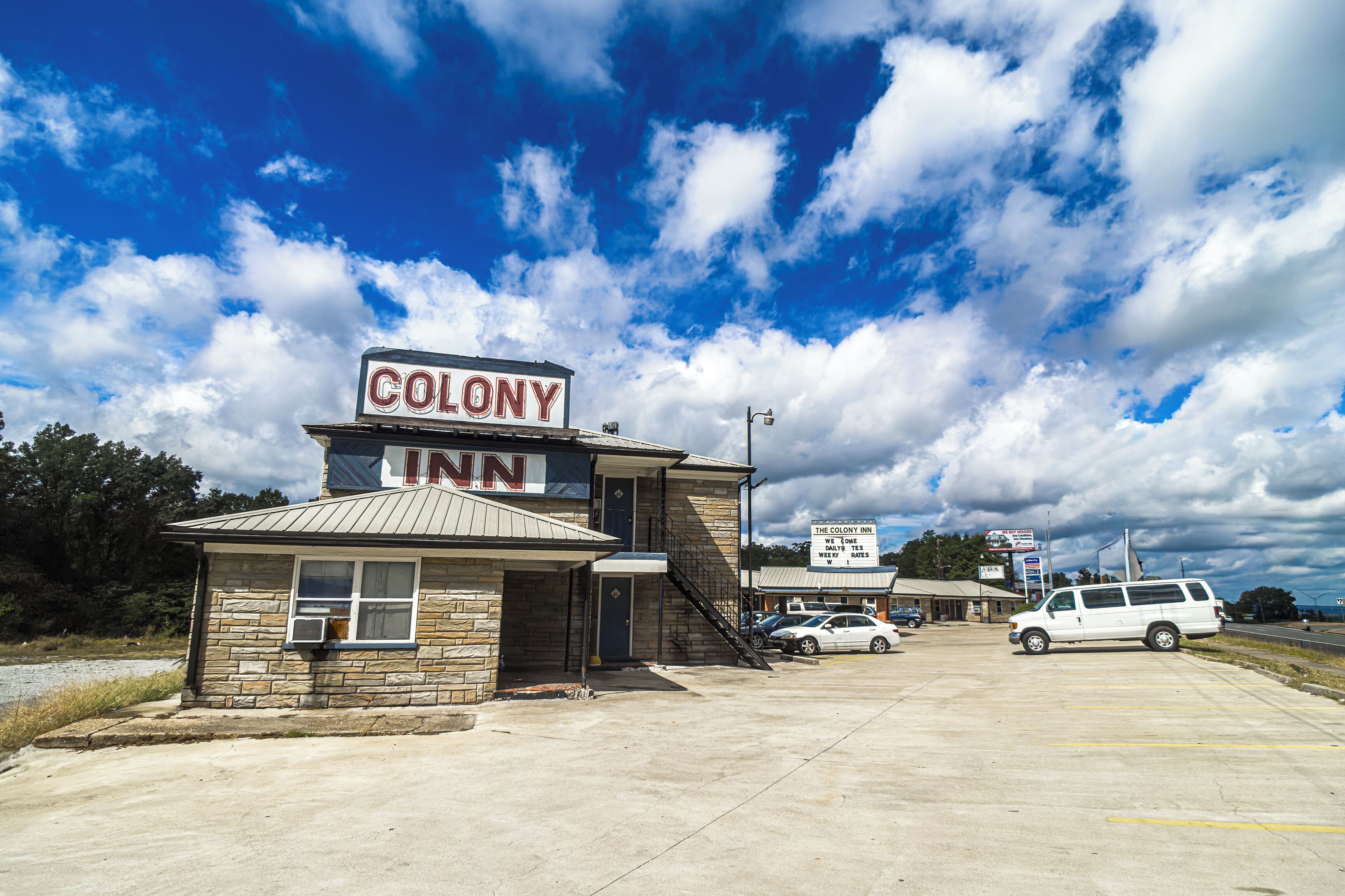 A two-story building with a sign reading 'Colony Inn' and a parking lot with several cars.