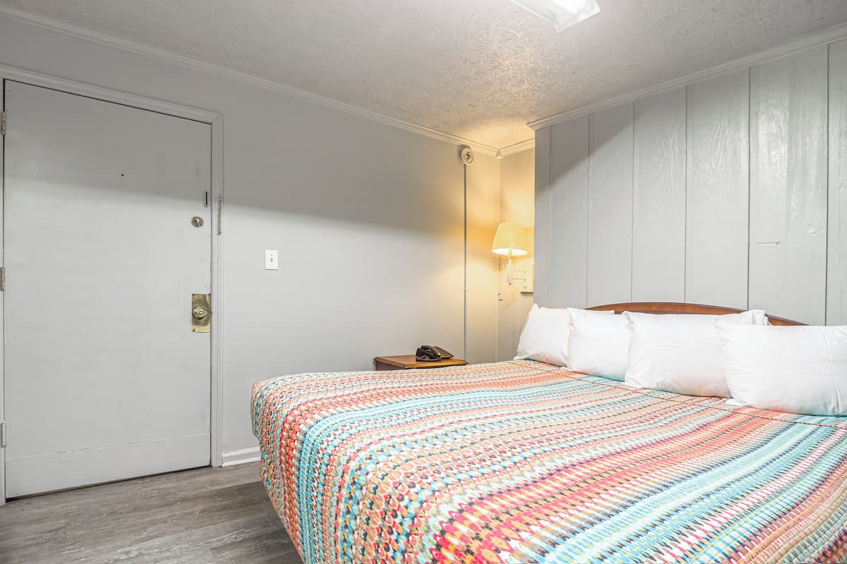A hotel room with a bed, a nightstand, a lamp, and a door.