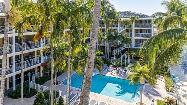 A multi-story hotel with a central swimming pool surrounded by palm trees and lounge chairs. - Boca Waterfront • Walk to Beach • Pool & Hot Tub • Gym • Parking (Boca Raton)