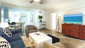 A modern living room with a ceiling fan, a large flat-screen TV, and a view of the ocean. - Boca Waterfront • Walk to Beach • Pool & Hot Tub • Gym • Parking (Boca Raton)